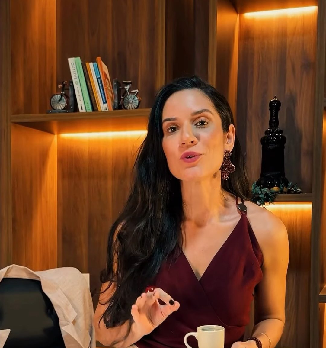 Dra. Kemilly Prates em pé no consultório, segurando uma xícara de café