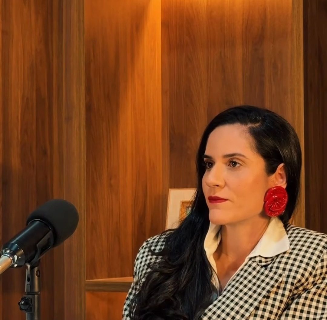Dra. Kemilly Prates no consultório, com estante de madeira iluminada ao fundo